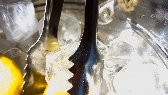 Silver tongs gripping ice cube with slice of lemon