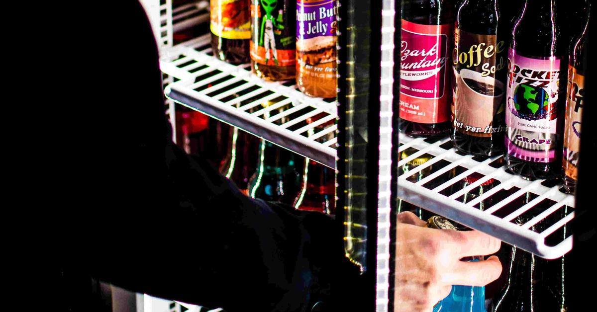 bottle cooler with door open and person stocking bottles inside on white wire shelves