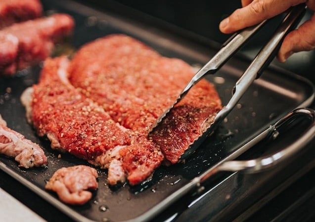 meat cooking on hot plate with hand holding cooking tongs