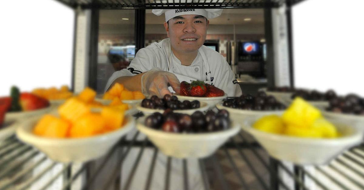 front facing image of a chef placing bowls of fruit on a wire shelf