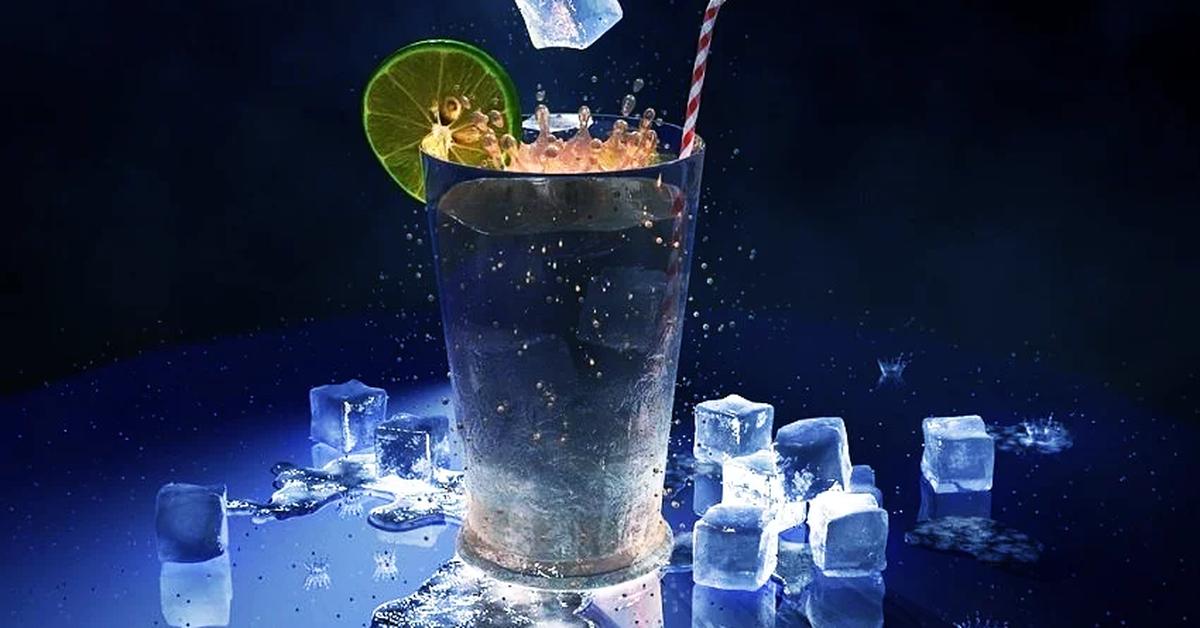 glass with drink, straw, lime slice and ice cubes around it